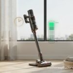 Aspirador vertical sem fio na base de carregamento com indicador de bateria ilustrado em verde mostrando progressão de carga e ícone de relógio dourado representando autonomia